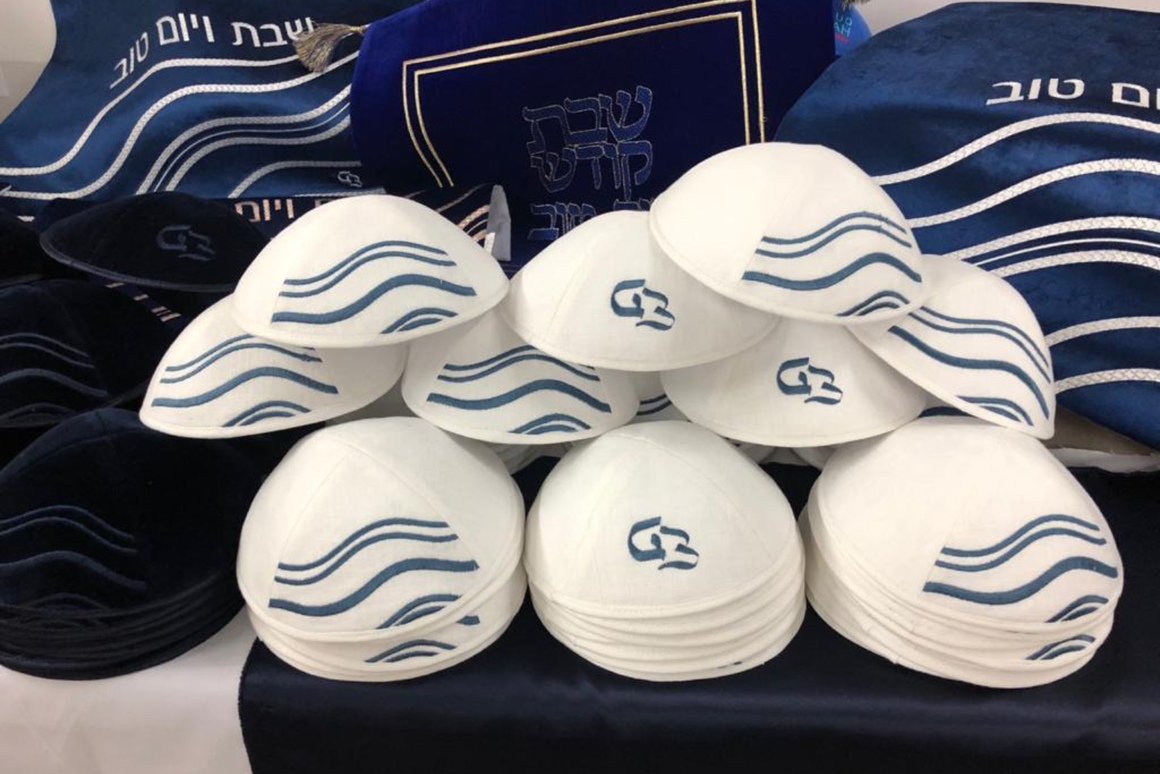 Kippas blanches personnalisées avec motif vagues bleues brodées, présentées avec des accessoires de cérémonie.