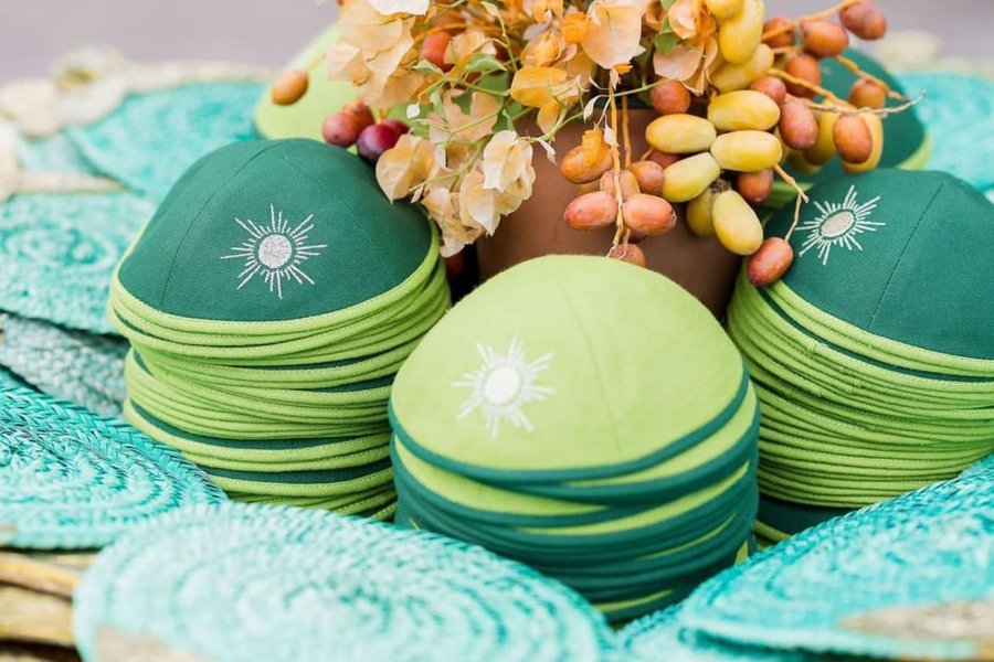 Kippas vertes personnalisées avec motif soleil brodé, disposées sur une décoration florale aux tons naturels.