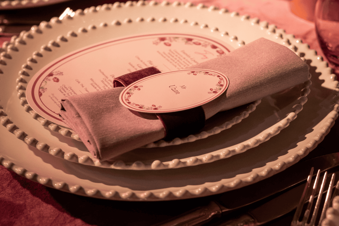 Menu de mariage personnalisé avec décoration florale rose et mauve, présenté sur une assiette blanche avec serviette assortie et rond de serviette violet.