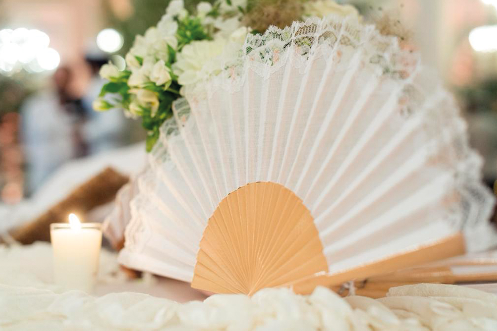 Éventail de mariage blanc en dentelle avec monture en bois naturel, présenté sur une table de réception.